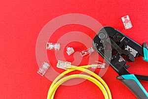 Computer network laying concept. Crimper tool and transparent connectors connectors on red background. Crimper and ethernet cable