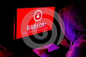 Computer screen with ransomware attack alerts in red and a hacker man keying on keyboard in a dark room, ideal for online