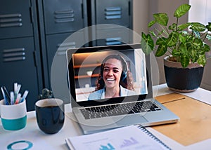 A computer shows a woman on a conference call, with hybrid work office and home photo
