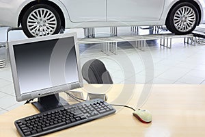 Computer stands on wooden desk and new car stands in office