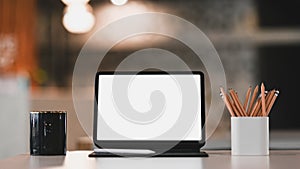 Computer table with blank screen, coffee cup and pencil holder on white office desk.