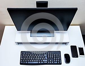 Computer wireless mouse, black monitor, keyboard and two mobile phones on a white desk.