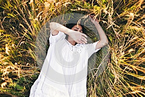 Conceived Beautiful young woman lying in the grass, wearing a white dress. Nature, summer holidays, vacation and people