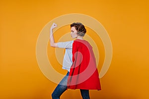 Concenrated girl with short hair looking at muscles. Indoor photo of serious female model in red mantle showing her