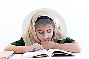 Concentrate Muslim student girl with beautiful eyes wears traditional hijab costume, study and do homework on table kid read book