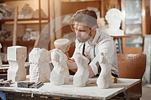 Concentrated 30-aged creative bearded stonemason knocks off from limestone needed shape of future sculpture using wooden