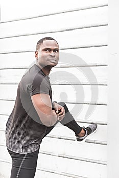 Concentrated african american sportsman warming up and stretching legs on pier, pulls up on a horizontal bar