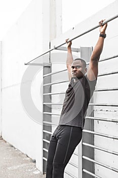 Concentrated african american sportsman warming up and stretching legs on pier, pulls up on a horizontal bar