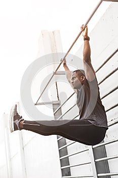 Concentrated african american sportsman warming up and stretching legs on pier, pulls up on a horizontal bar