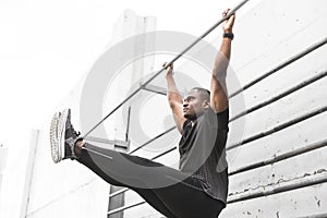 Concentrated african american sportsman warming up and stretching legs on pier, pulls up on a horizontal bar