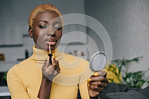 Concentrated african american woman applying lip gloss and looking photo