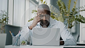 Concentrated african man employee american expert focused specialist sits in office works on laptop use personal