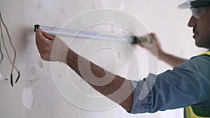 Concentrated architect in protective helmet measuring wall with white tape-line