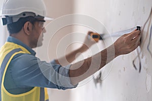 Concentrated architect in protective helmet measuring wall with white tape-line