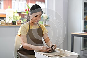 Concentrated Asian woman creating handmade ceramic bowl in a pottery on the pottery wheel in workshop. Activity