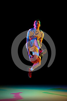 Concentrated athlete man, basketball player dribbling against black studio background in mixed neon light. Model