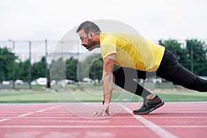 Concentrated athlete standing in low start pose before sprint on red rubberized track in city