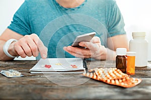 Concentrated attentive man pointing at pills holding the cellphone.