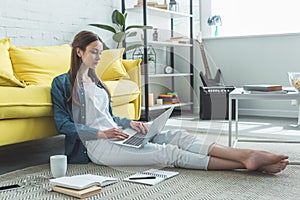 concentrated barefoot girl using laptop while sitting on carpet and studying