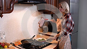 Concentrated beautiful woman frying asparagus in kitchen at home. Side view portrait of blond confident Caucasian lady