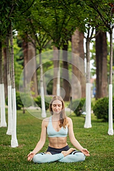 Beautiful young woman practicing yoga in park and making namaste mudra