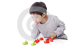 Concentrated boy plays paper ships on table