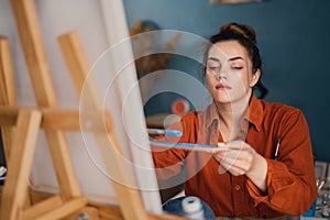 a concentrated Brazilian woman artist with paint on her hands works on drawing a picture on canvas sitting in front of