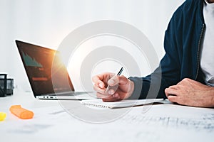 Concentrated building designer working with drawing plan and competer while sitting by the table at studio office