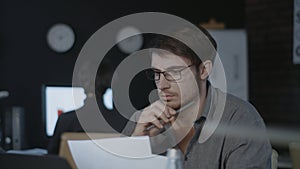 Concentrated business analyst watching document and laptop screen in dark office