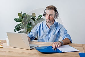 Concentrated businessman in headphones working with documents and laptop in office