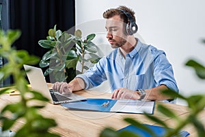 Concentrated businessman in headphones working with documents and laptop in office
