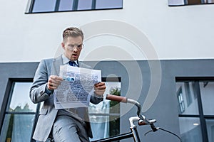 Concentrated businessman reading newspaper near bike
