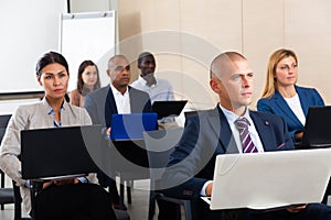 Concentrated businesspeople working on laptops during corporate seminar