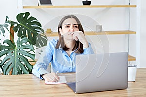 Concentrated businesswoman is doing paperwork while sitting with a laptop at the table at home, focused senior employee preparing