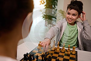 Concentrated Caucasian school boy developing chess strategy, thinking on chess movement while playing with his mother. Logic