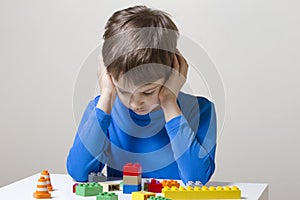 Concentrated child sitting and looking down to colorful plastic construction toy blocks at the table