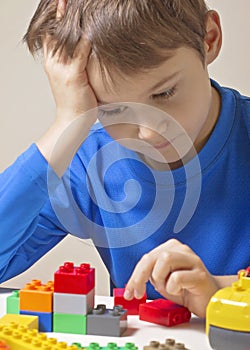 Concentrated child sitting and looking to colorful plastic construction toy blocks at the table