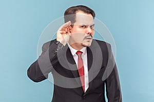 Concentrated curious man with mustache standing with hand near ear, listening private information.