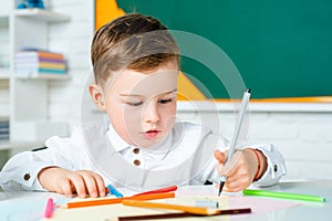 Concentrated cute child, writing in notebook using pencil. Cute child is sitting at a desk indoors.