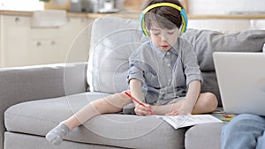 Concentrated cute preschool boy in headphone draw in notebook listen lesson for homeschool education