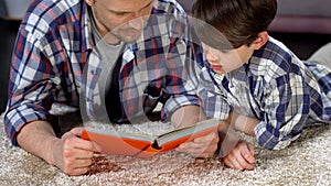 Concentrated dad and son reading interesting encyclopedia for boys, education