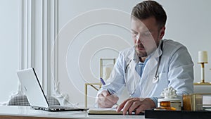 Concentrated doctor working with laptop at desk in office. Male doctor using laptop at desk in clinic