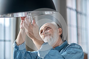 Concentrated elderly man changing a lightbulb in his lamp