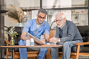 Concentrated elderly person and his caretaker perusing news