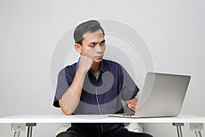 concentrated face of asian man while sitting in front of laptop computer. on isolated bakcground
