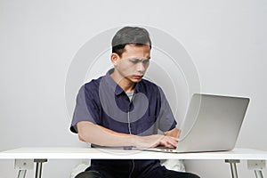 concentrated face of asian man while sitting in front of laptop computer. on isolated bakcground