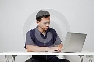 concentrated face of asian man while sitting in front of laptop computer. on isolated bakcground