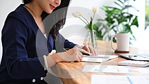 Concentrated female accountant taking notes on notebook and working with financial document