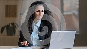 Concentrated female arab businesswoman multitasking worker accountant calculate costs credit balance use laptop online