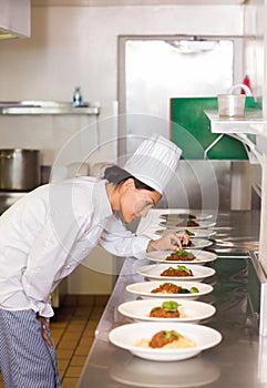 Concentrated female chef garnishing food in kitchen